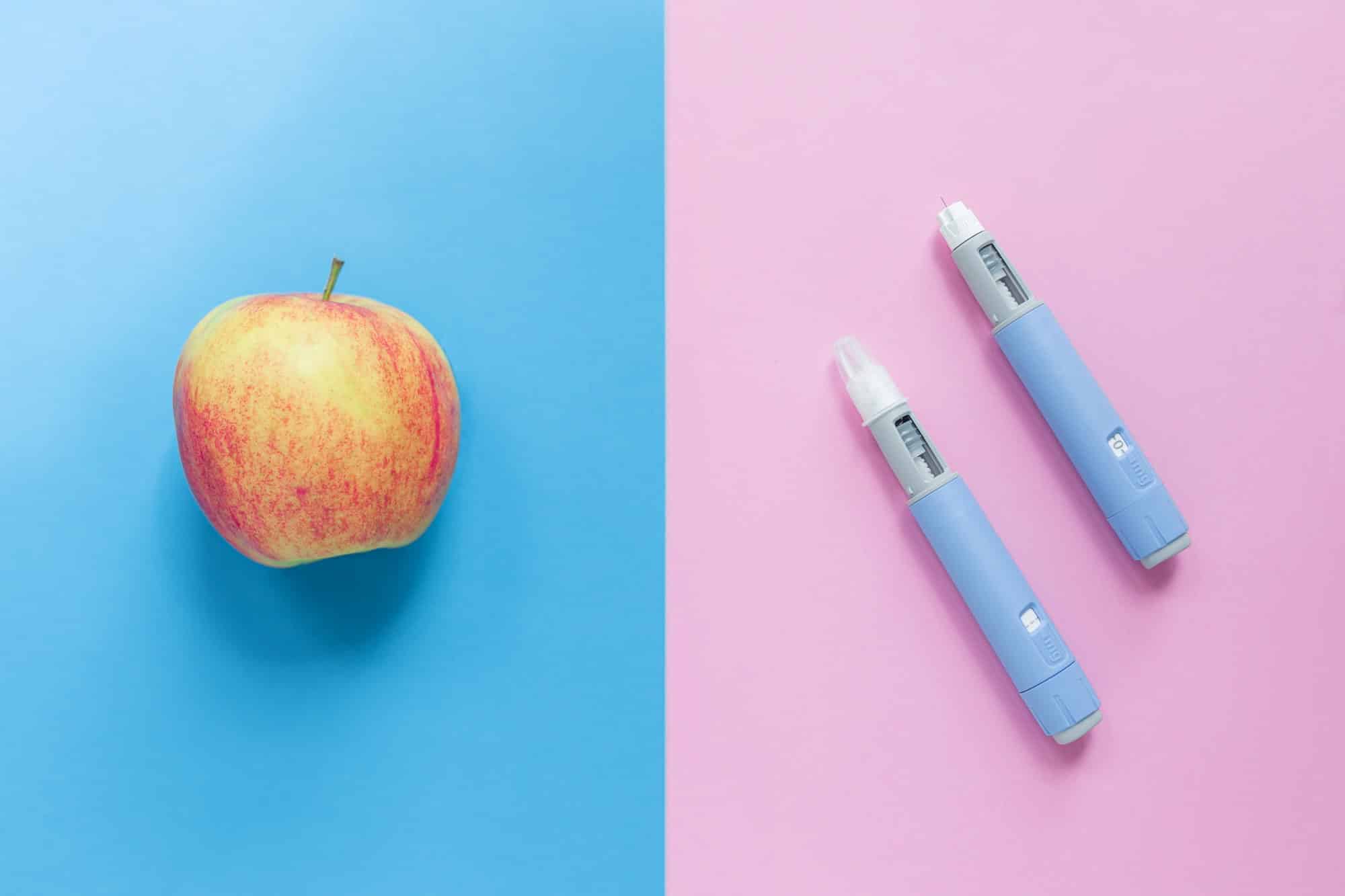 Delicious apple on a blue background and two injectors dosing pens for subcutaneous injection