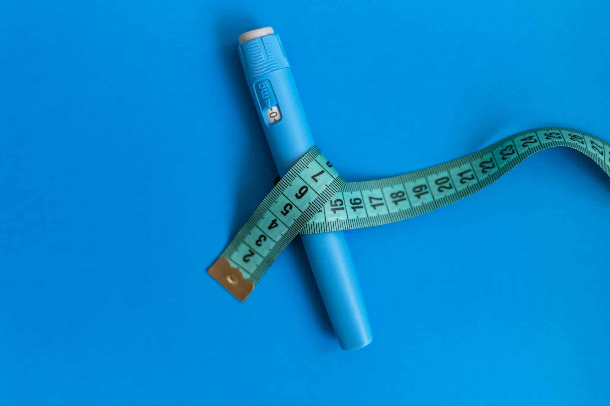 Ozempic injector drug with a measuring tape on a blue background.