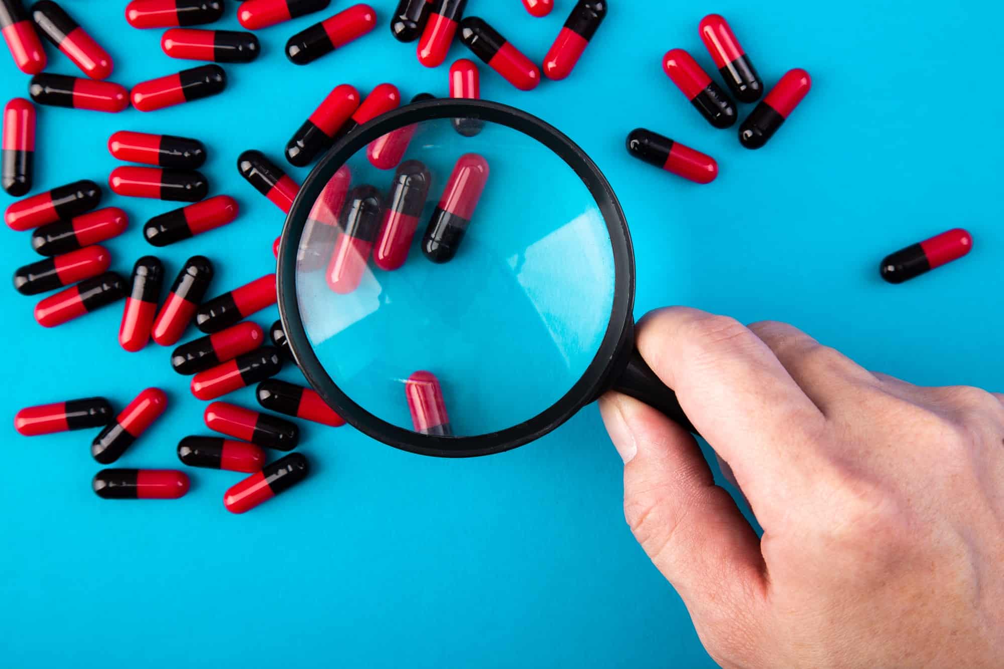 hand with a magnifying glass looking at pills