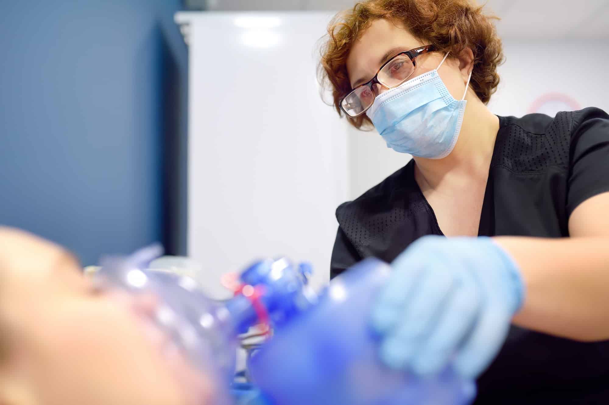 A nurse puts on an oxygen mask with positive pressure on a patient lying in the intensive care